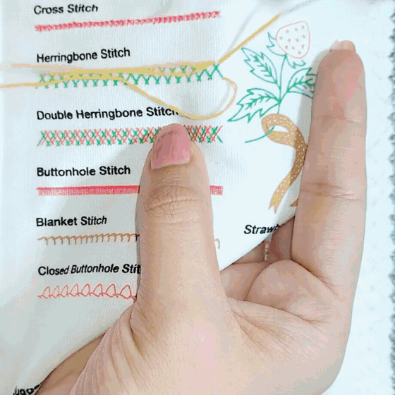 Hands stitching a running stitch on a bound linen page of the Emberly embroidery stitch book, no hoop
