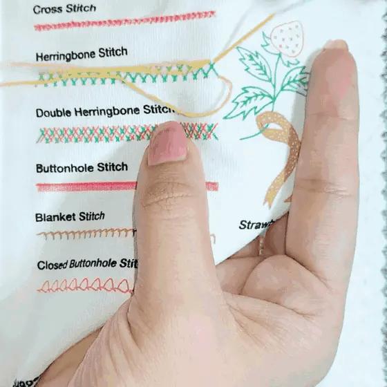 Hands stitching a sampler page of embroidery patterns